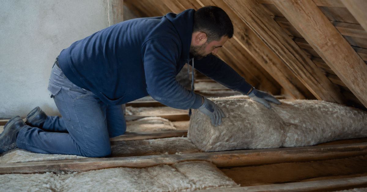 Ouvrier posant isolation fibreuse entre poutres combles