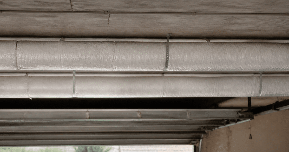 Rouleaux isolants blancs installes horizontalement sous plafond beton garage