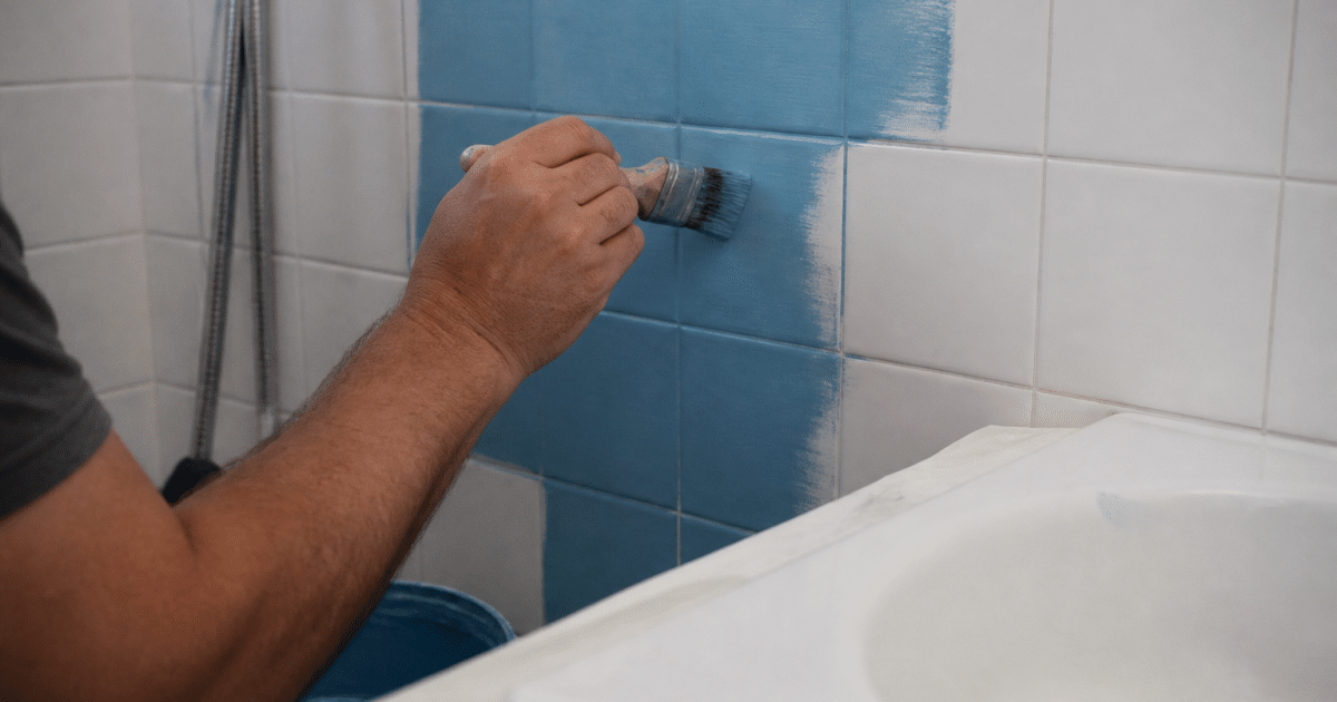 Main appliquant peinture coloree sur carrelage blanc salle bain